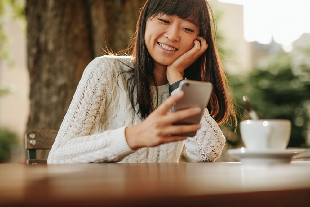 Asian woman smiling while holding smartphone.