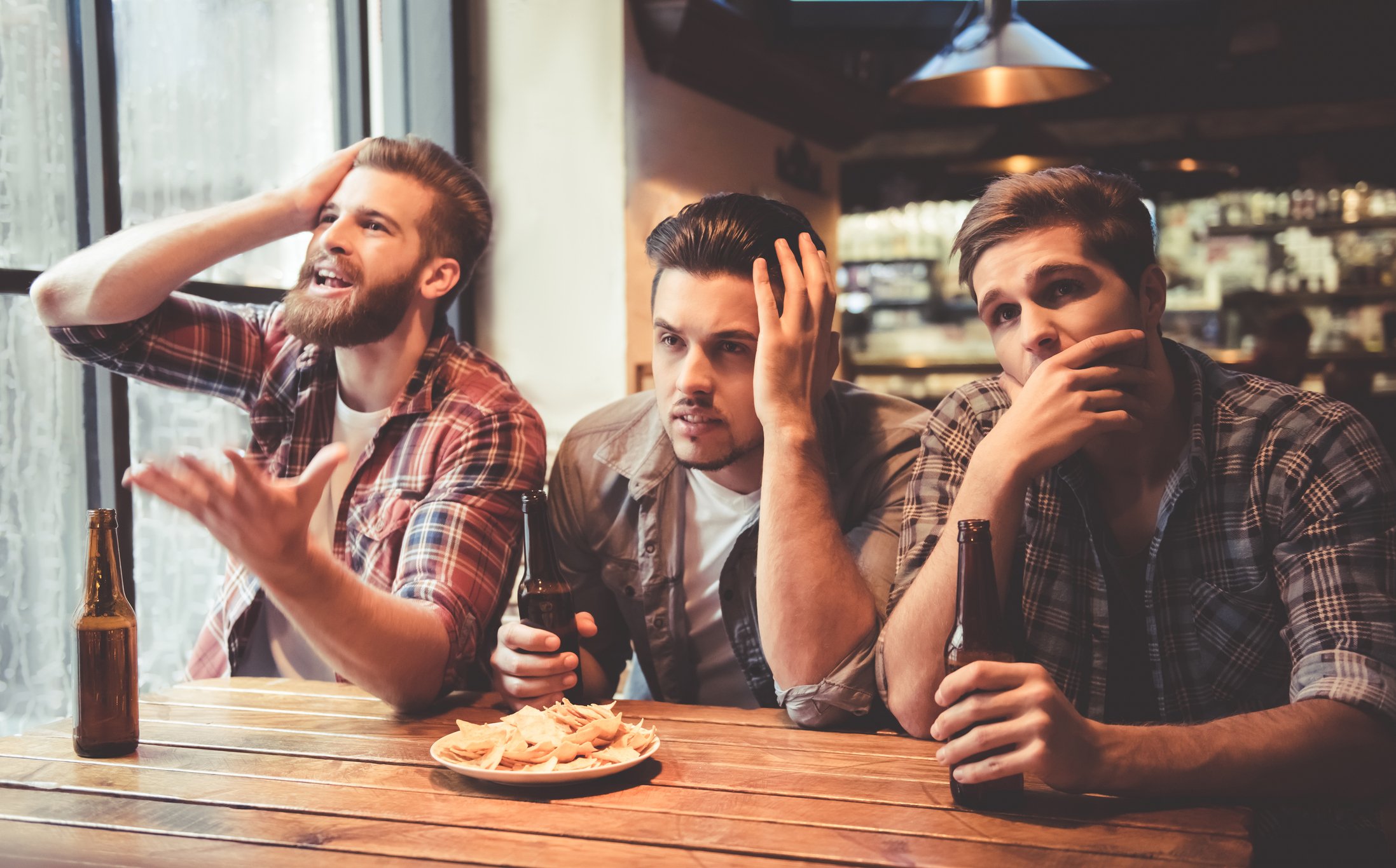 friends are sitting upset while drinking beer and cheering for sport team at the pub