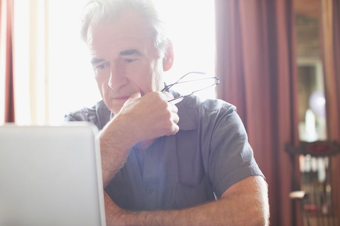 Older man at laptop with eyeglasses in hand