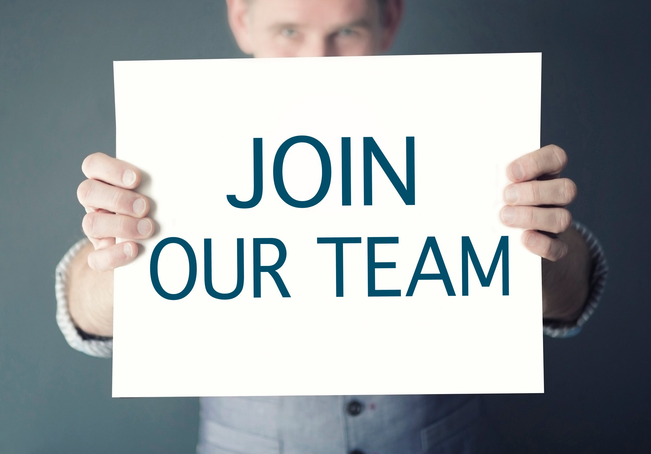 A man holds a sign that says "join our team."