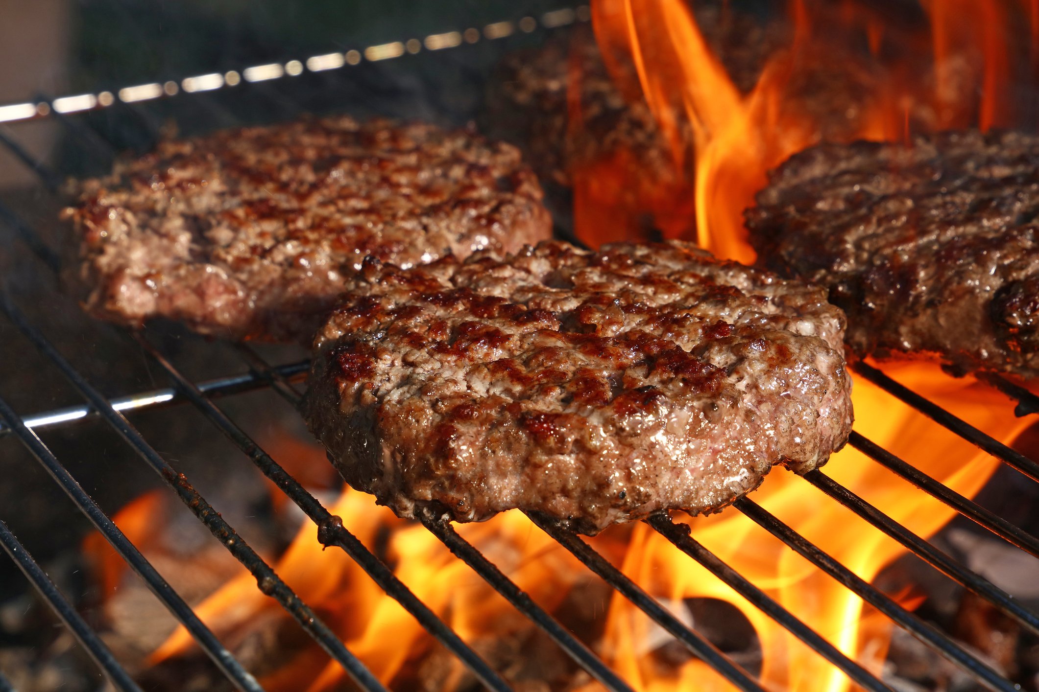 Several burger patties grilling over an open fire.