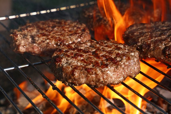 Several burger patties grilling over an open fire.