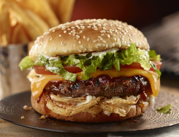 Burger with cheese, tomato, lettuce, and onion rings on a sesame seed bun