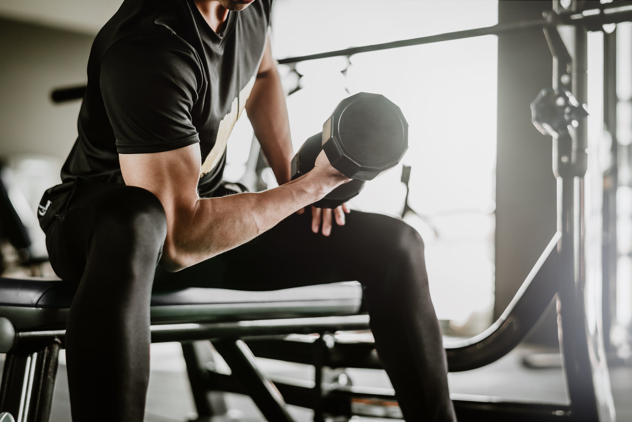 A man lifting a dumbbell while sitting on a weight bench.