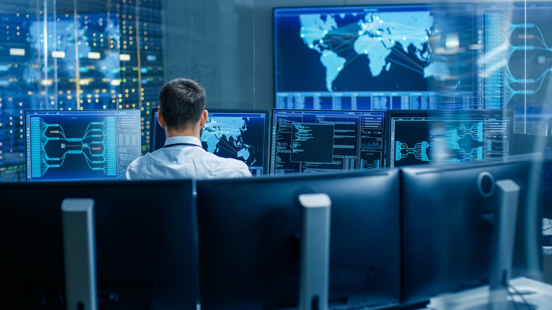 A man sitting in front of a computer surrounded by other computers in a network operations center.