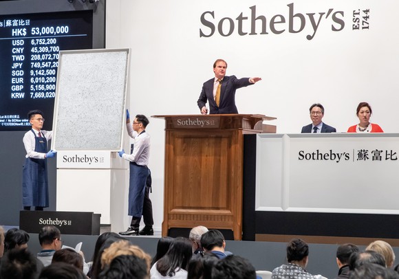 Person at podium pointing next to an artwork, with Sotheby's logo on back wall.