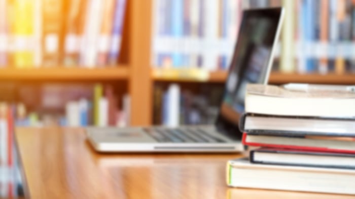 Books and laptop on a wooden table in a library.