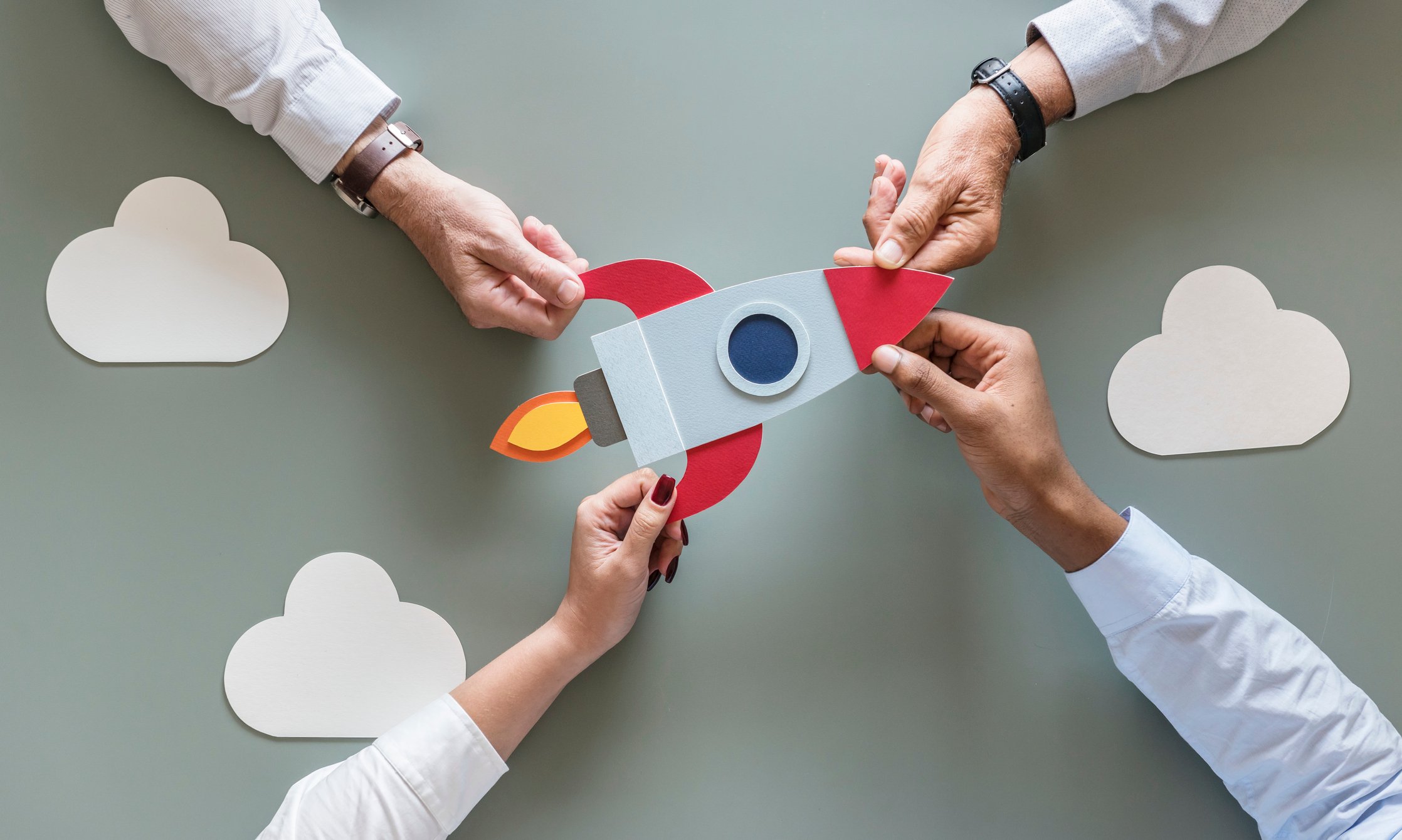 Four businesspeople hold a cardboard cutout of a rocketship to illustrate teamwork.