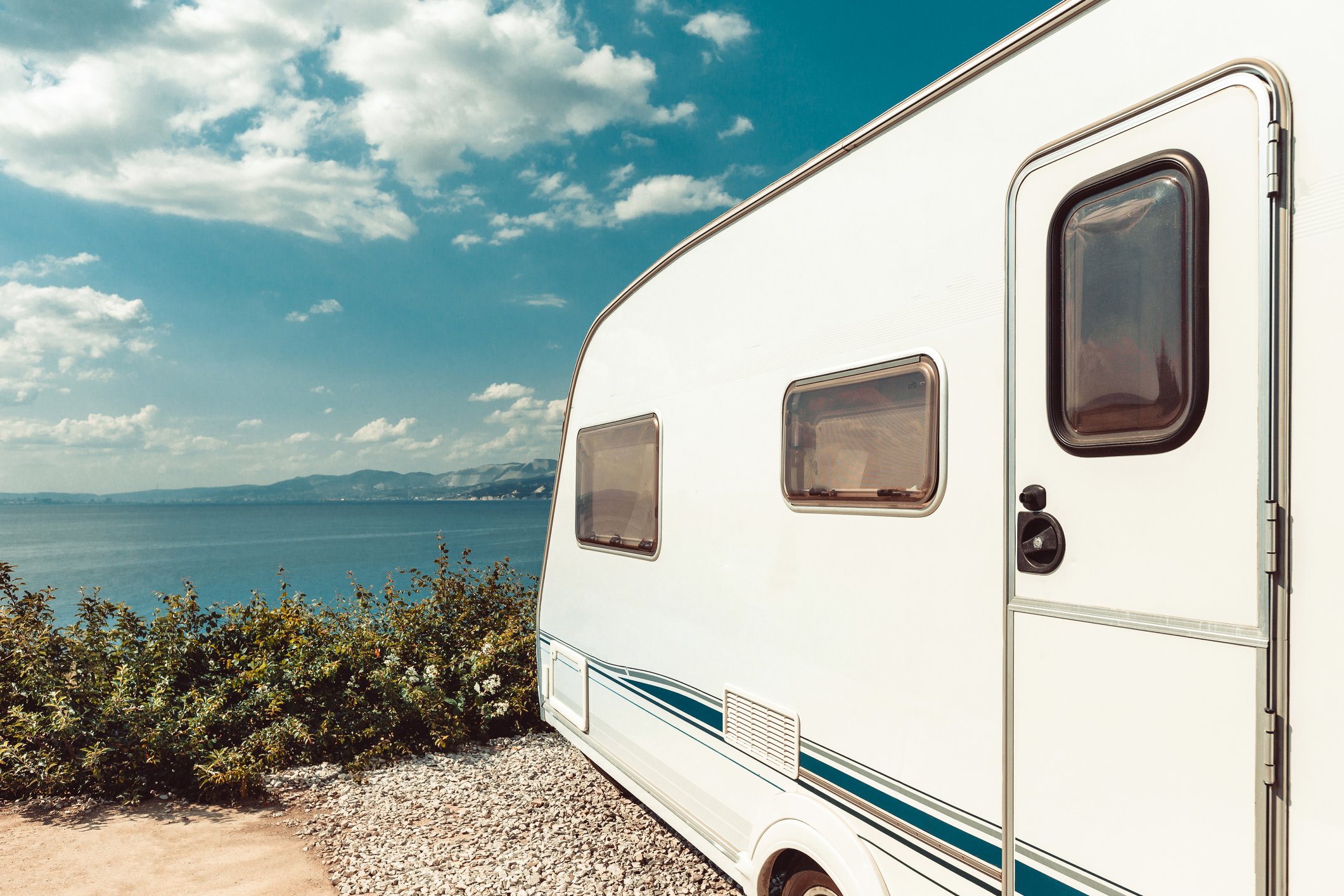 An RV camper parked near the beach under blue skies.