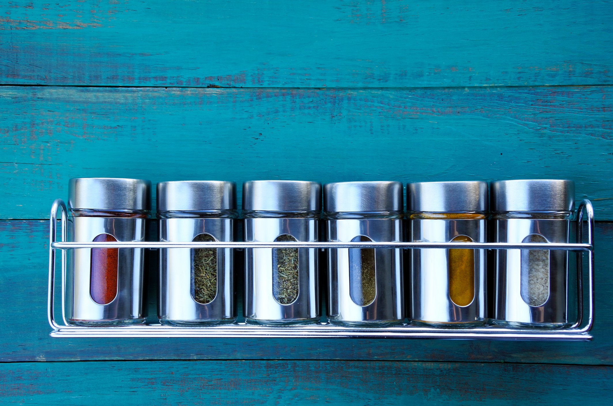 Steel spice rack hanging on a blue wooden wall.