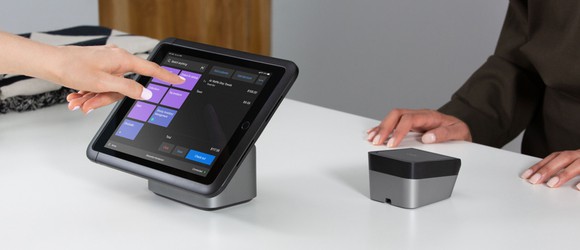 A merchant entering a sale on a tablet-based point-of-sale system, while a customer waits.