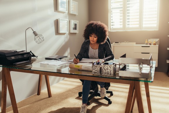 Woman writing at desk that appears to be set up in a home setting.