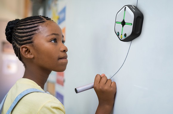 Young female student drawing a line for iRobot's Root coding robot to follow on a whiteboard.