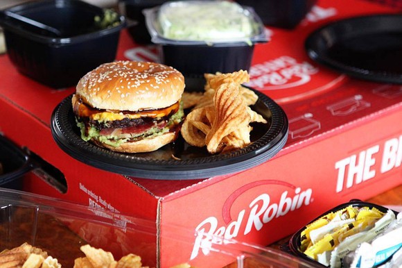 A burger and potato chips on a plate sitting on top of a Red Robin box