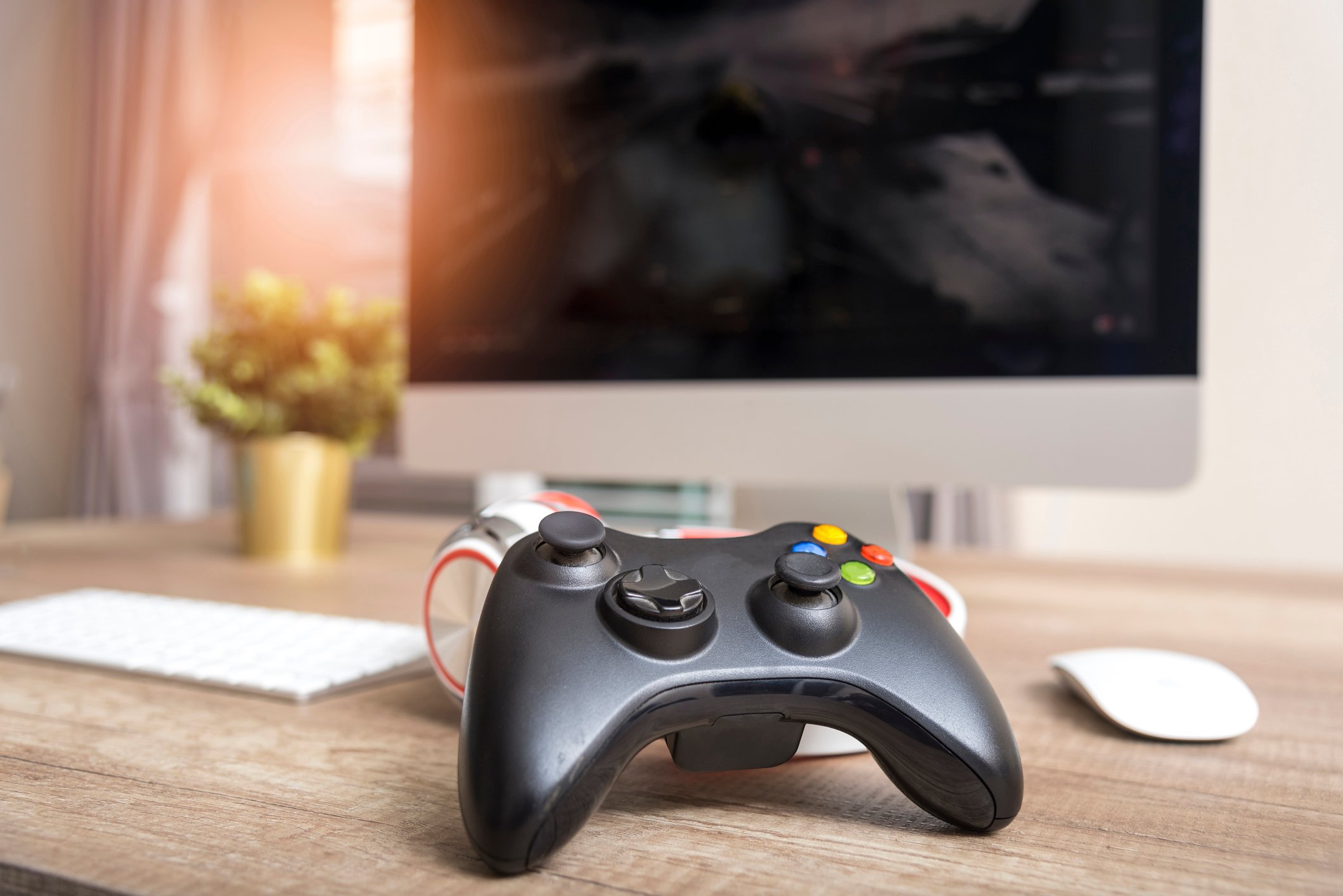 A video game controller lying on a desk with a desktop computer in the background.