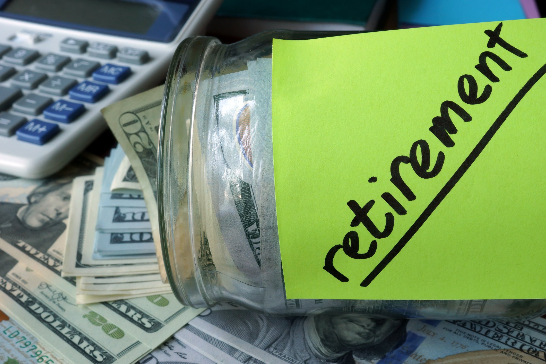 Glass jar holding cash with a note saying Retirement on the side, next to a calculator.