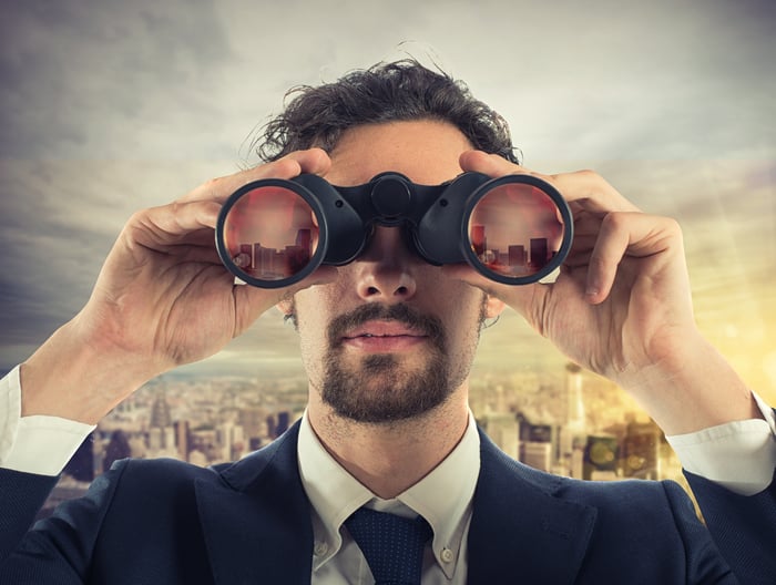 A man in a suit looking through a pair of binoculars.