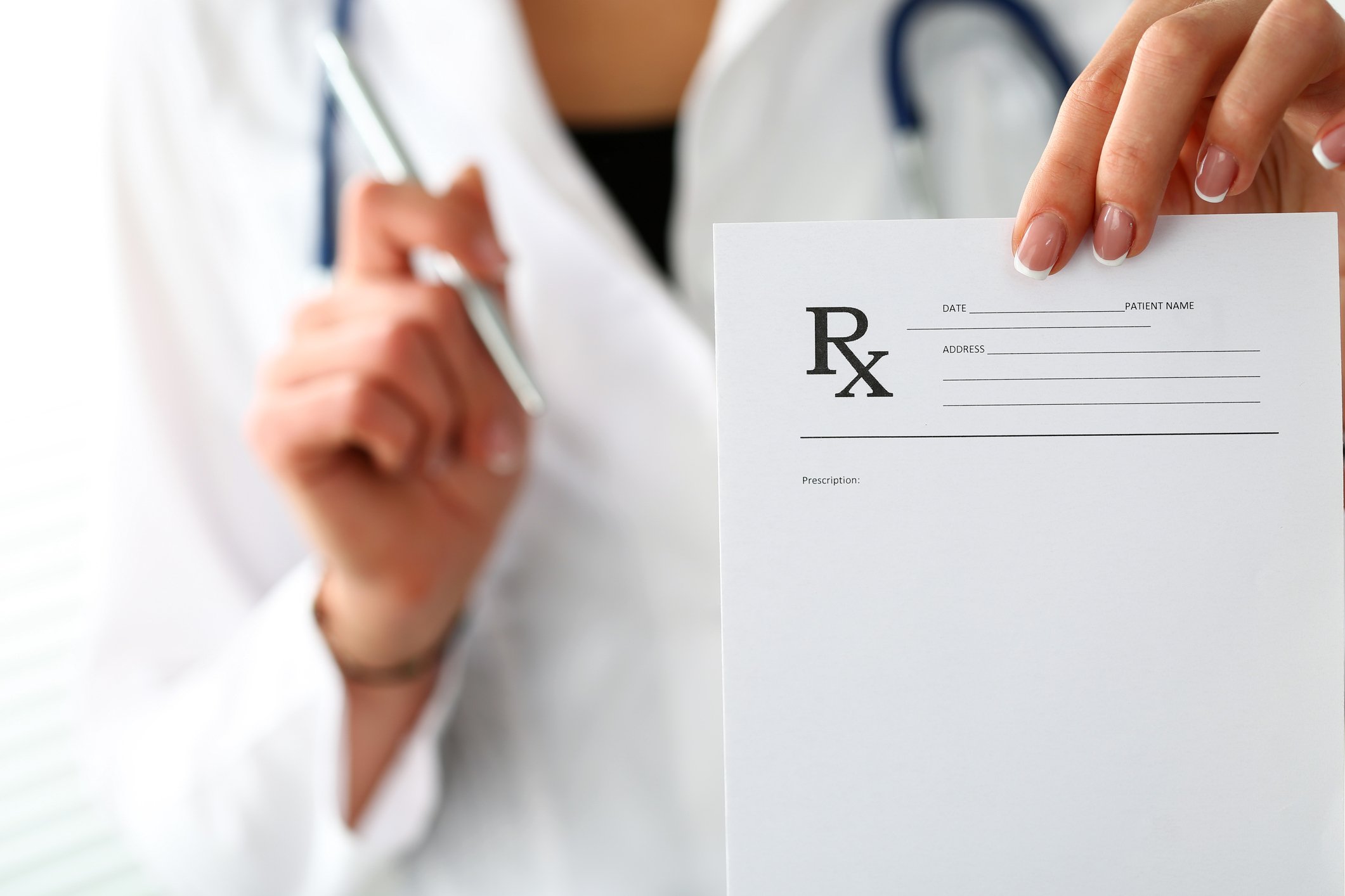 A female doctor holding out a prescription pad with her left hand and a pen with her right hand.