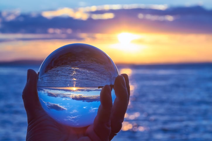 Hand holding a crystal ball in front of a body of water and sunset or sunrise. 