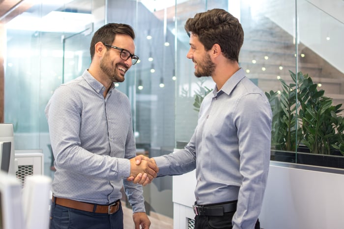 Two men in collared shirts shaking hands