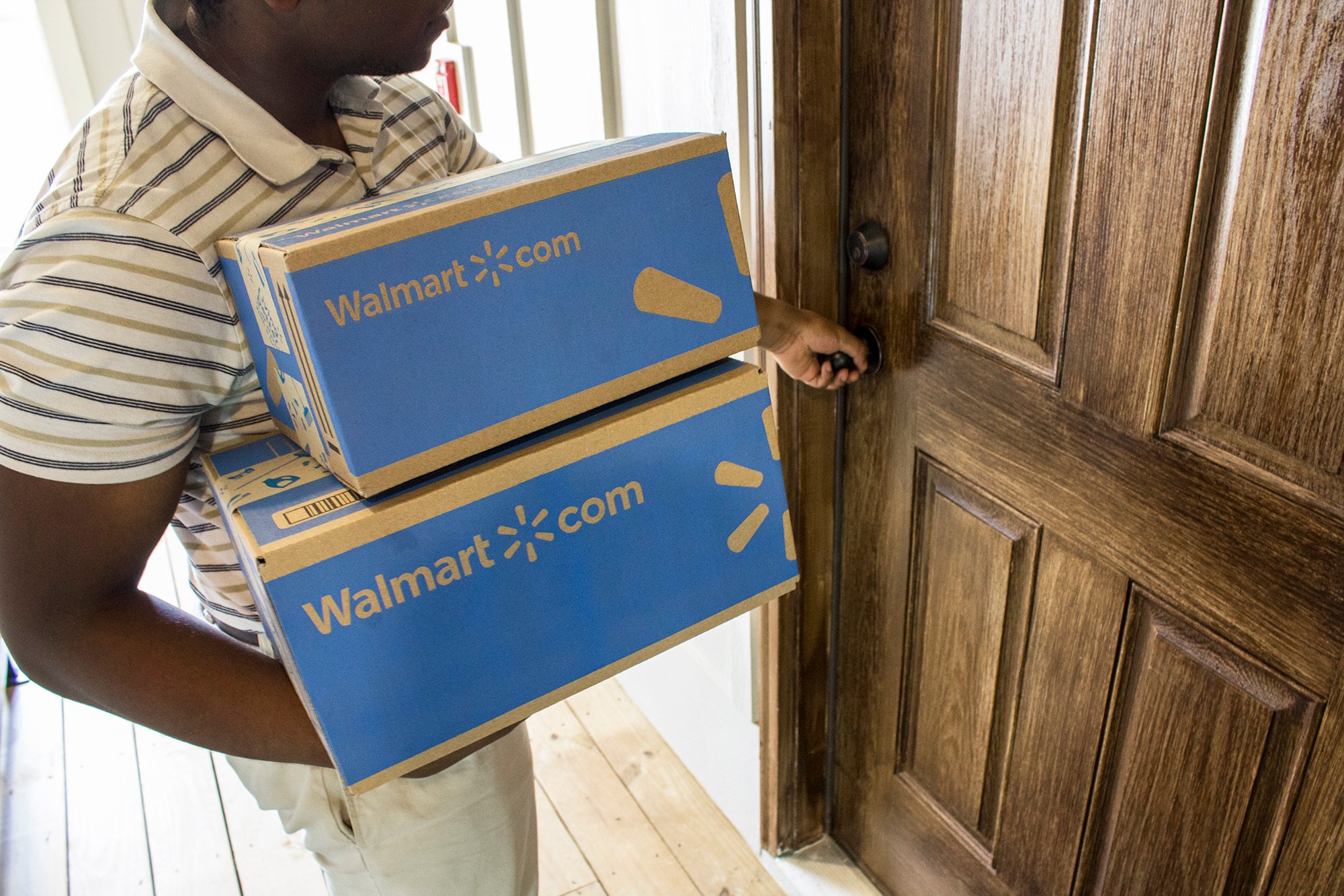 A man holding Walmart.com boxes and about to turn a doorknob.