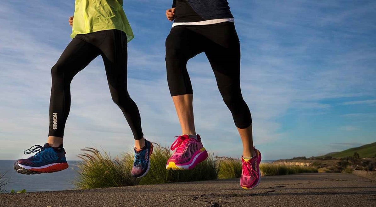 Two women running while wearing colorful Deckers shoes.