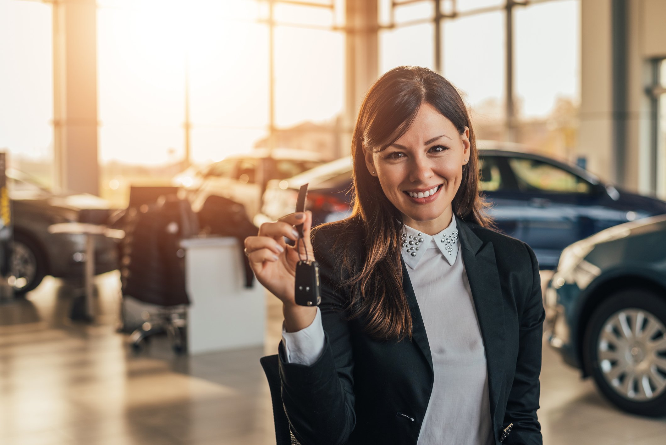 woman holding keys to a new car at a dealership