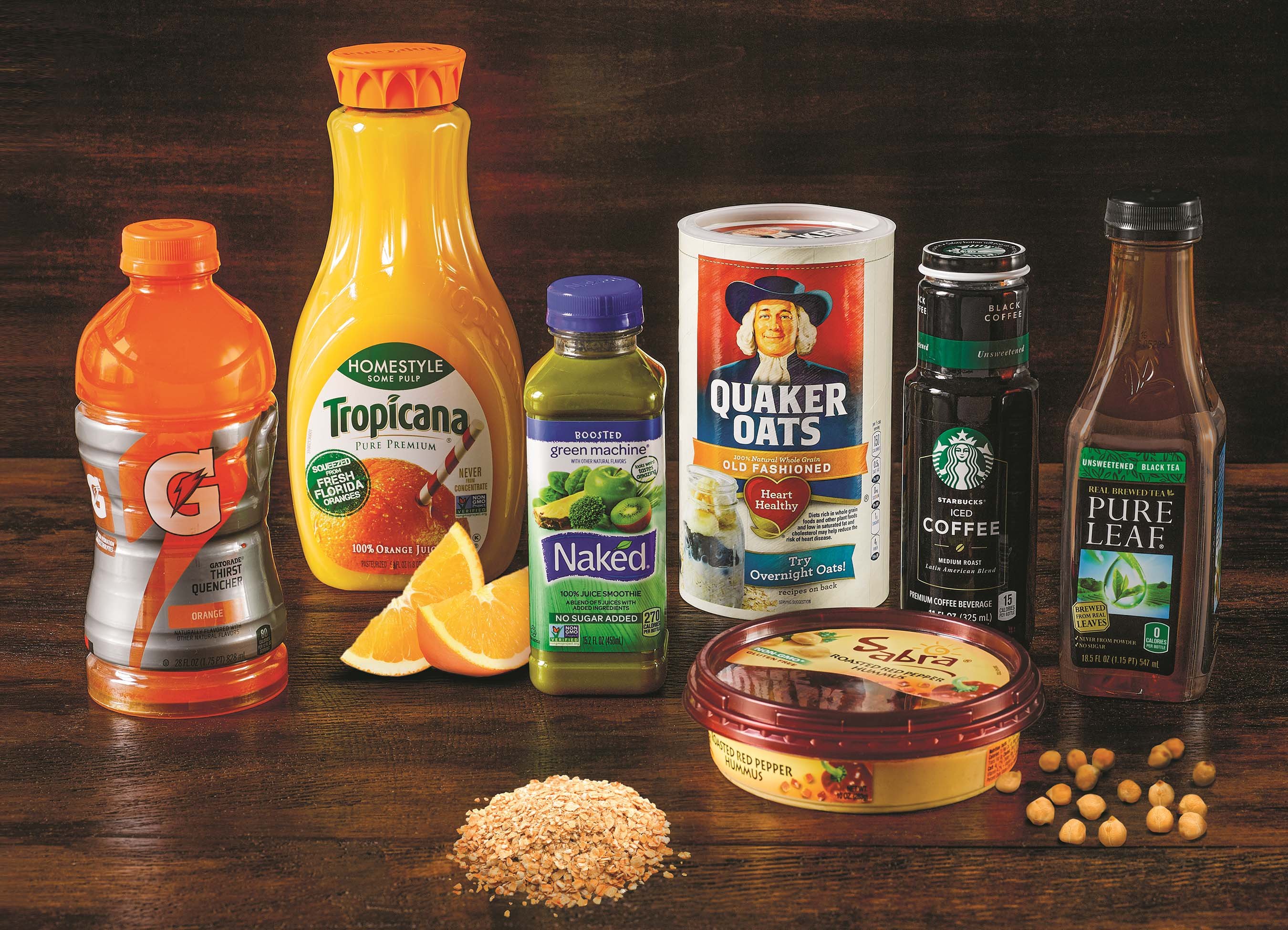 Various PepsiCo products on a wood table, including Gatorade, Tropicana orange juice, Quaker Oats, Sabra hummus, and others.