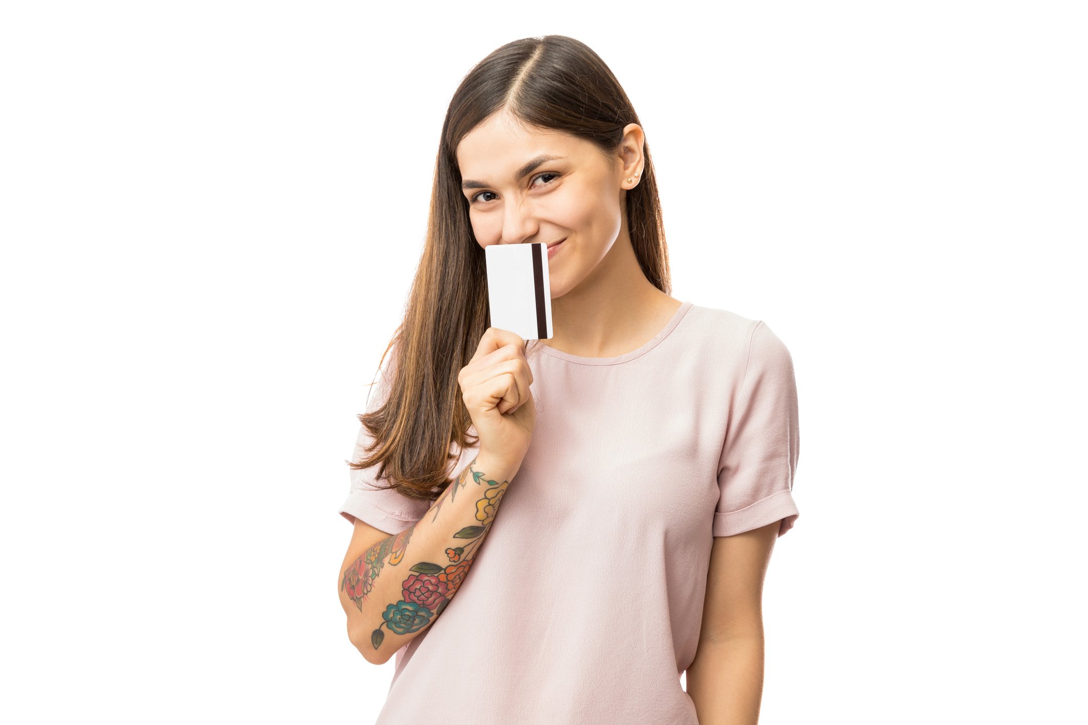 A young woman with a forearm tattoo smiles and holds a credit card to her nose.