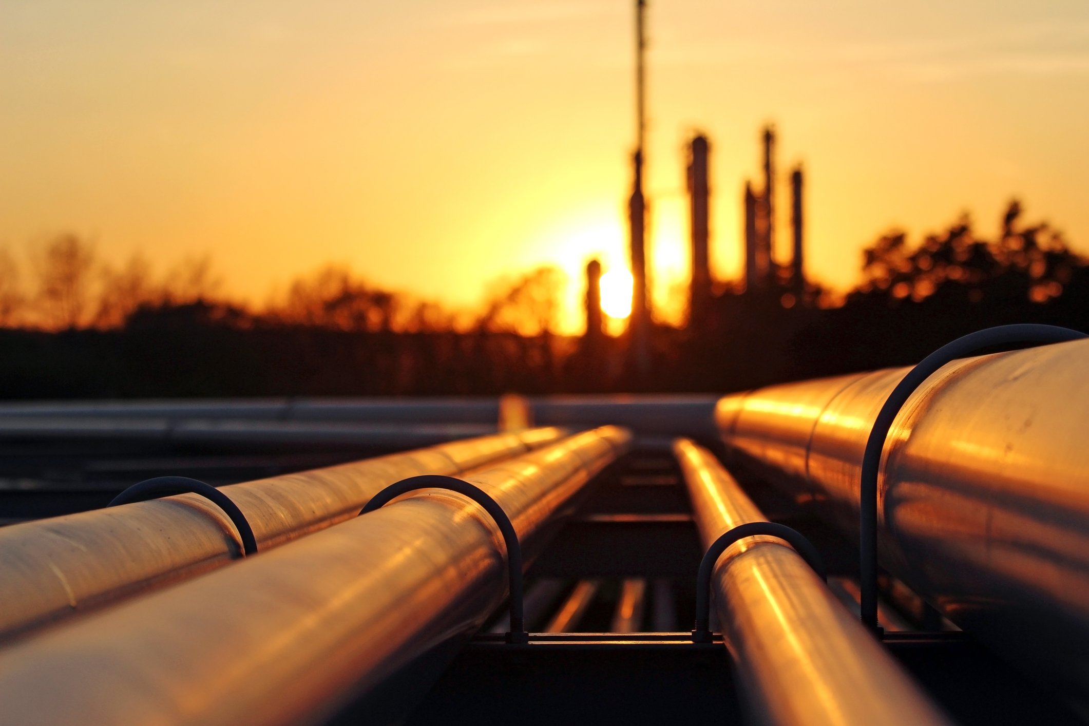 Pipeline pipes with a refinery in silhouette at sunset.