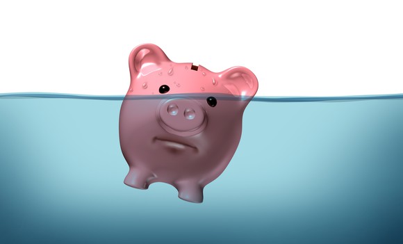 A piggy bank is shown, half submerged in water and with an unhappy expression.