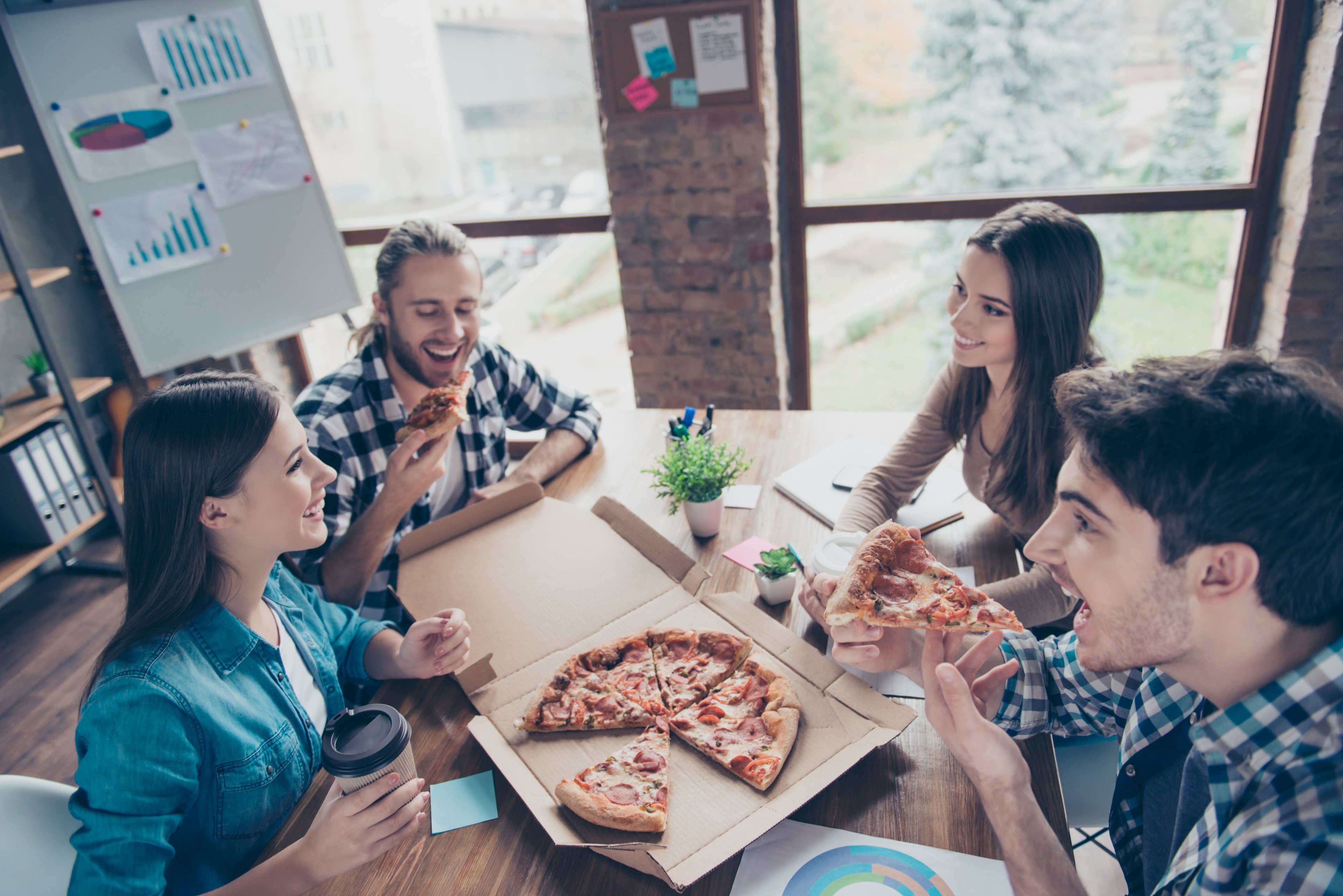 A group of people in an office eating pizza around a desk.