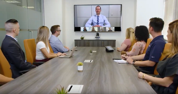 Several employees in a conference room in a Zoom Video video-conference with someone else.