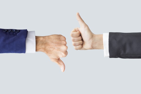 Two men's hands with one thumb down and one thumb up.