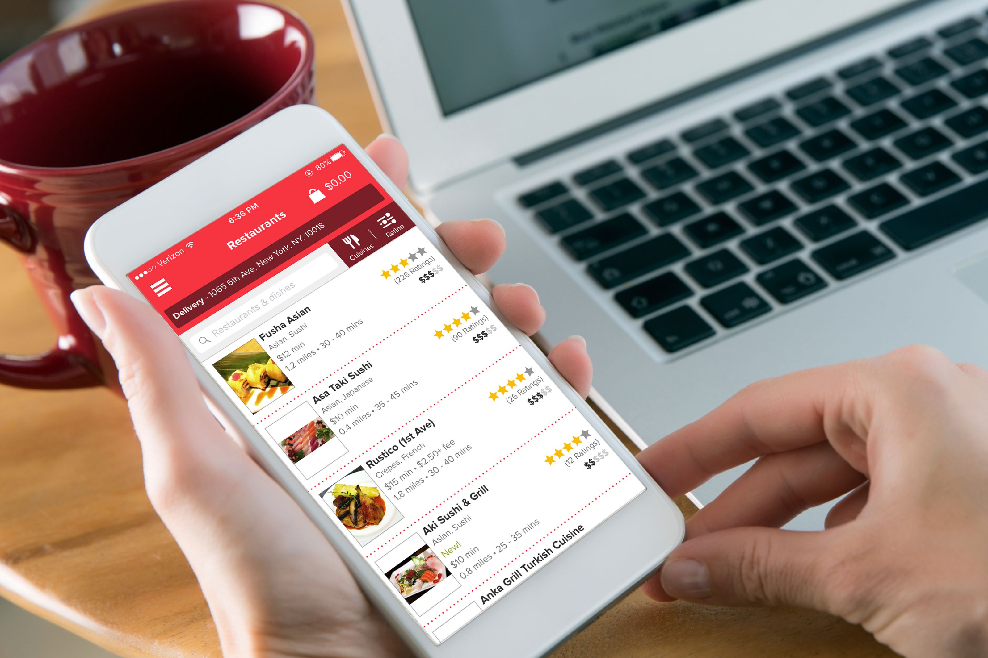 Grubhub's delivery app, as seen on a phone being held by a person above a laptop in the background.