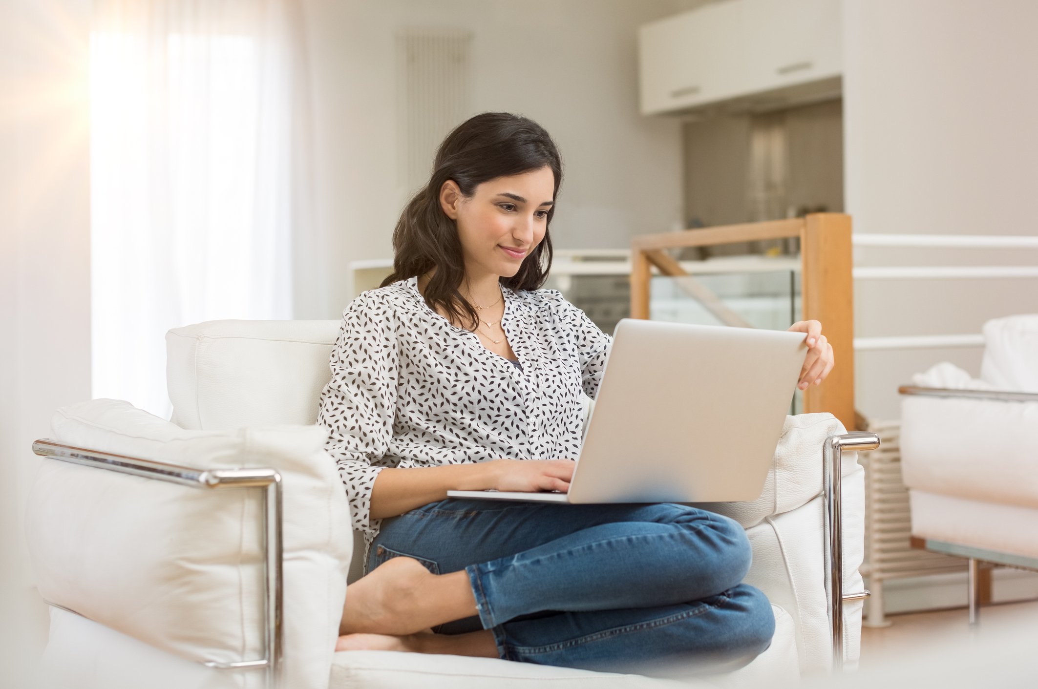 A woman sits on a couch holding a laptop.