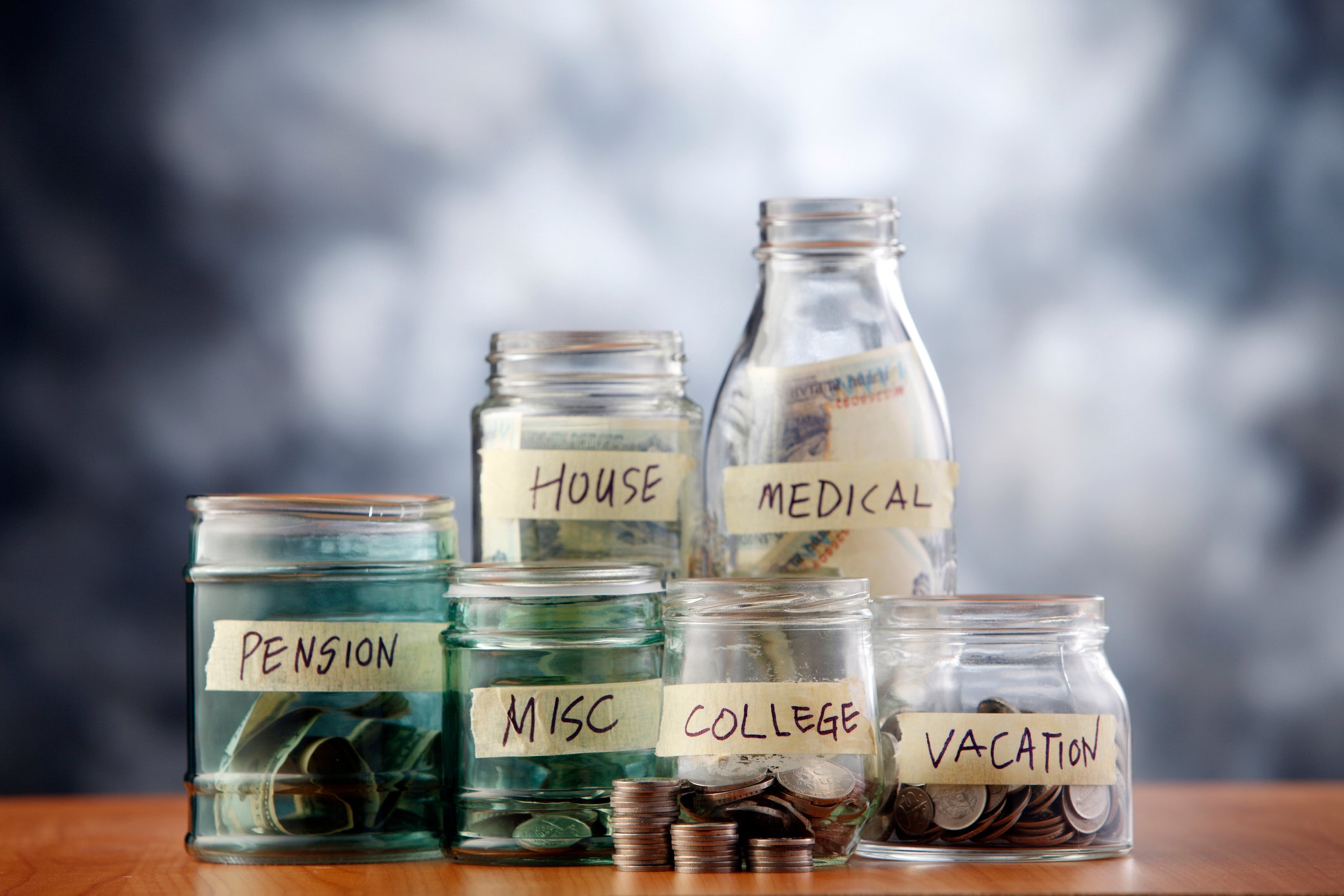 Labeled bottles for financial expenses, filled with bills and coins.