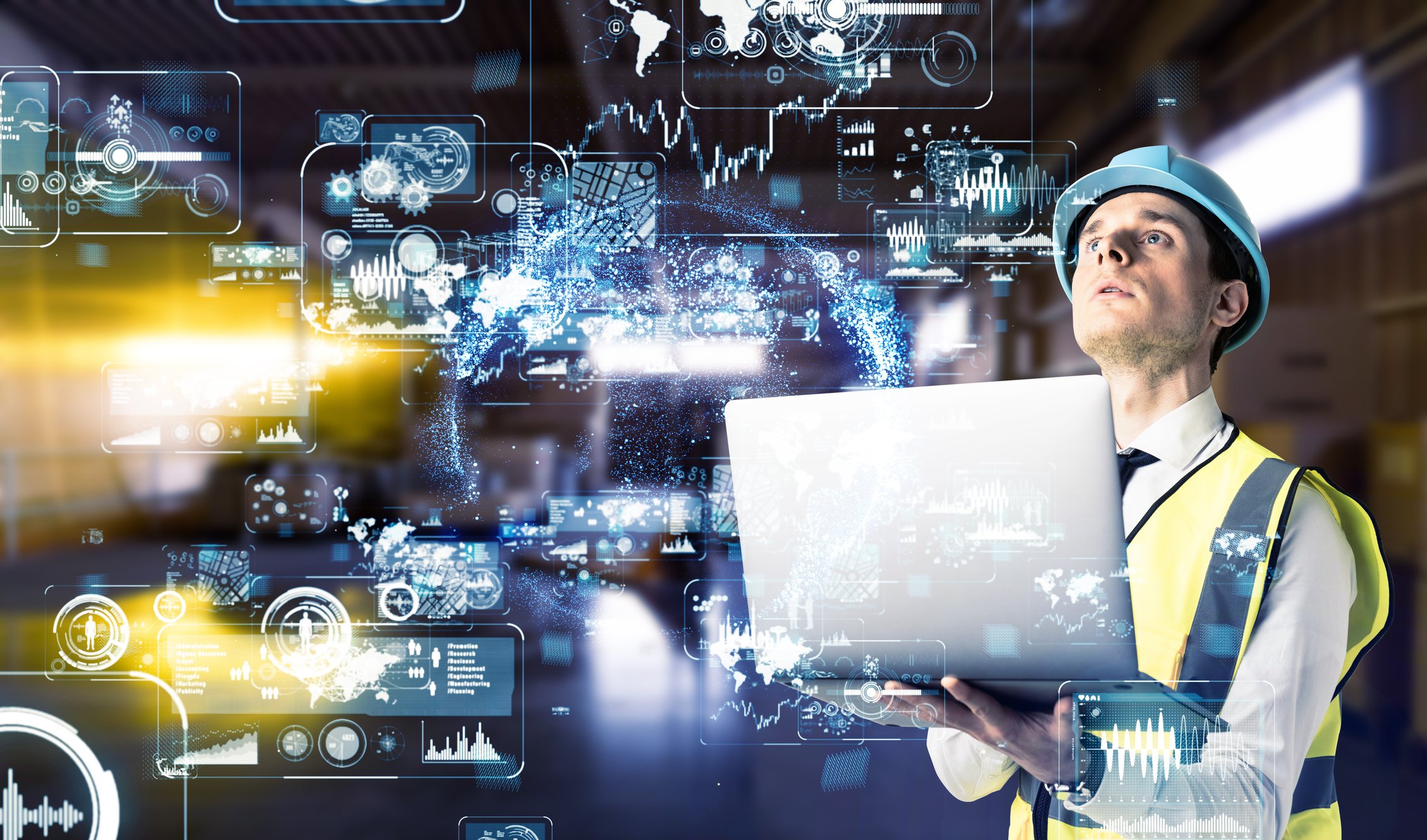 A worker in a hard hat holding a laptop and looking at digital industrial designs