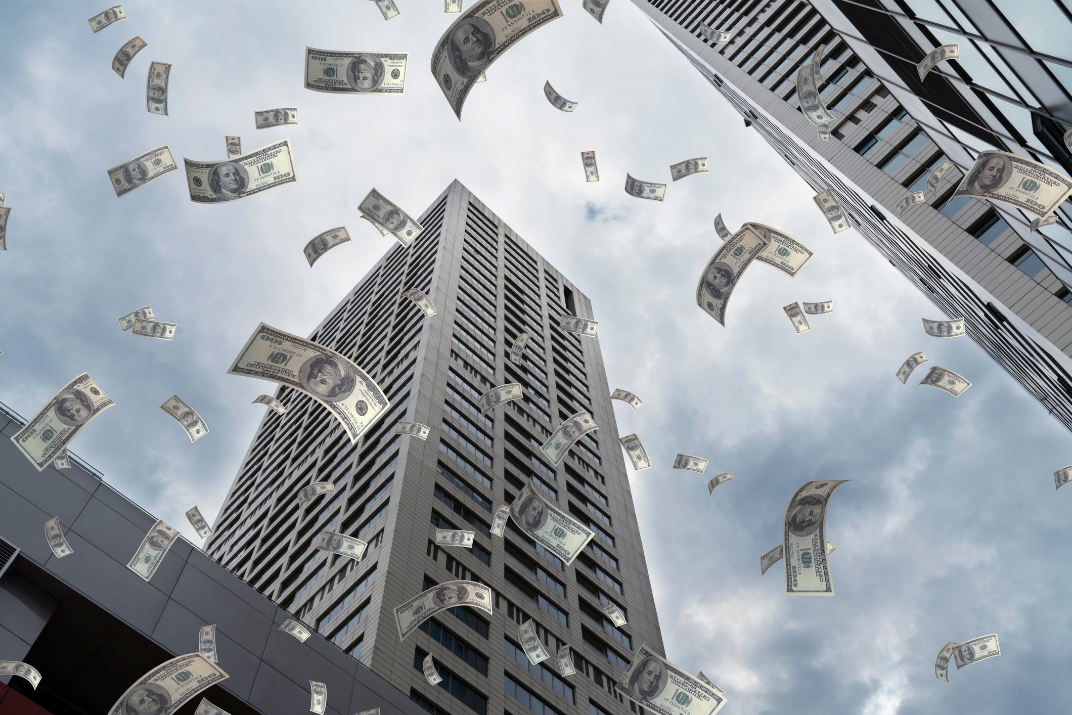 Dollars falling from the sky amid tall buildings.
