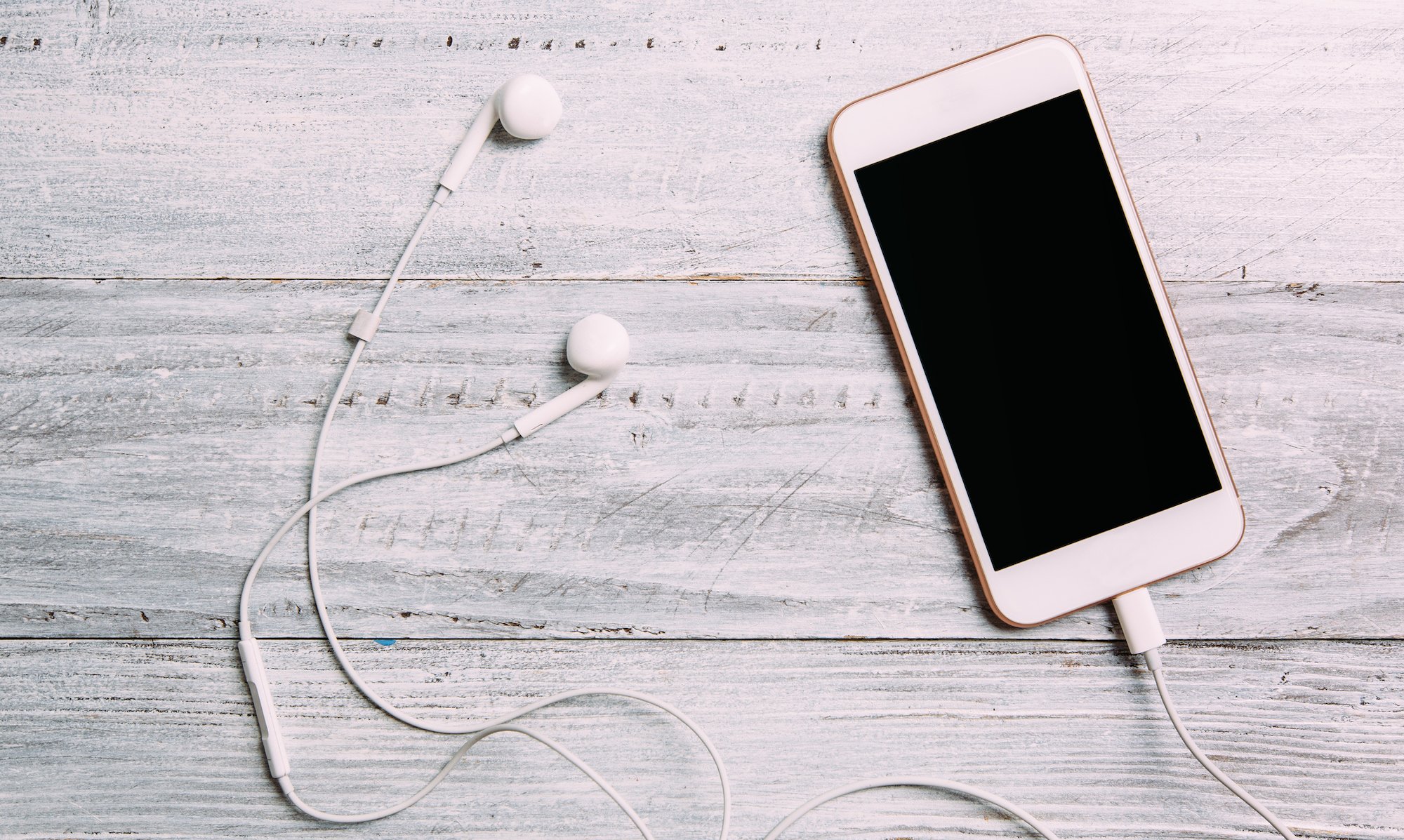 Phone sitting on a table with earbuds next to it.