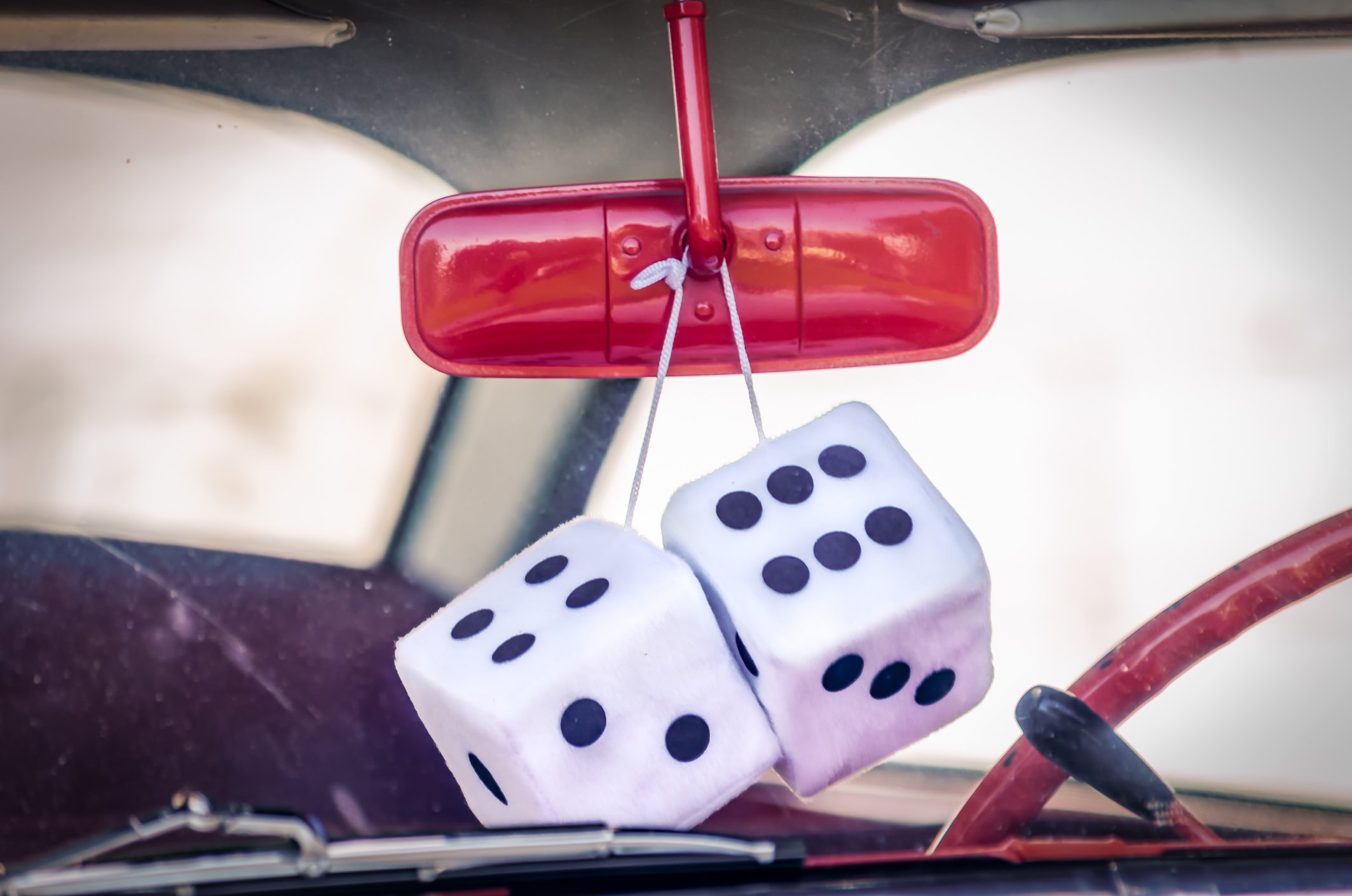 Fuzzy dice hang from a red rearview car mirror