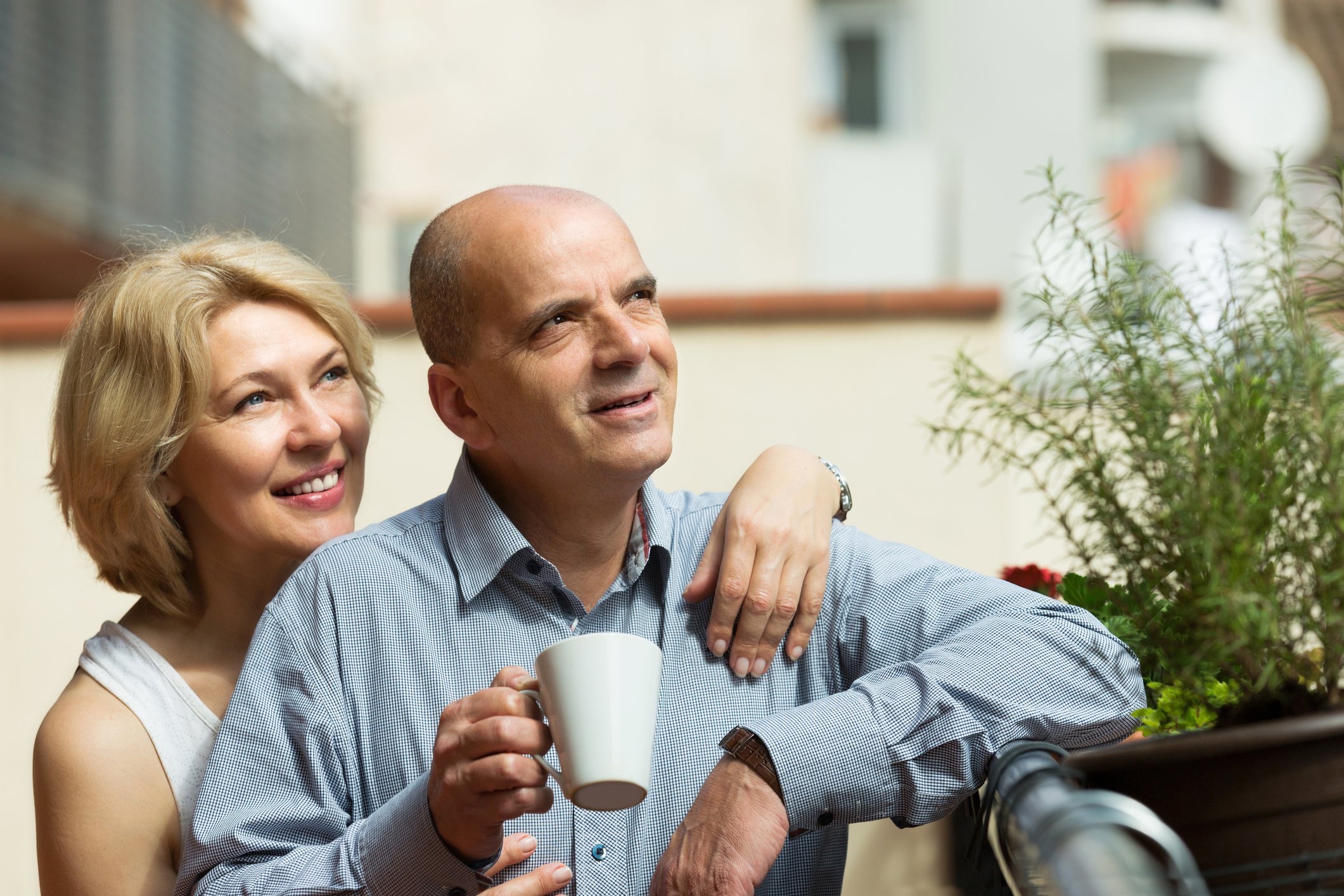 Middle-aged woman putting arm around middle-aged man holding mug