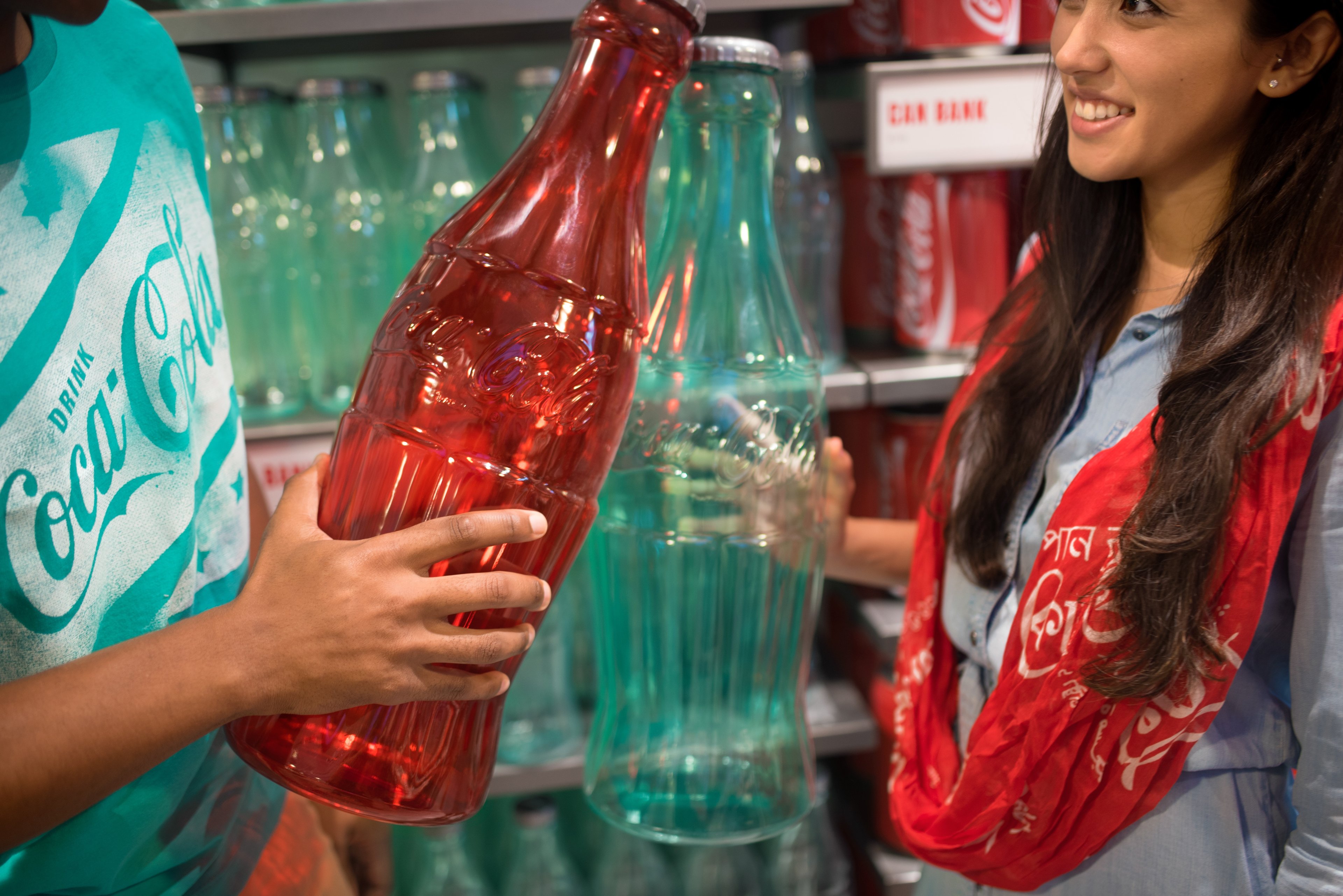 Two shoppers hold Coca-Cola bottle banks at the Coca-Cola store.