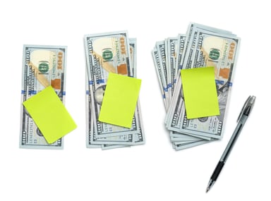 3 stacks of cash with sticky notes and pen