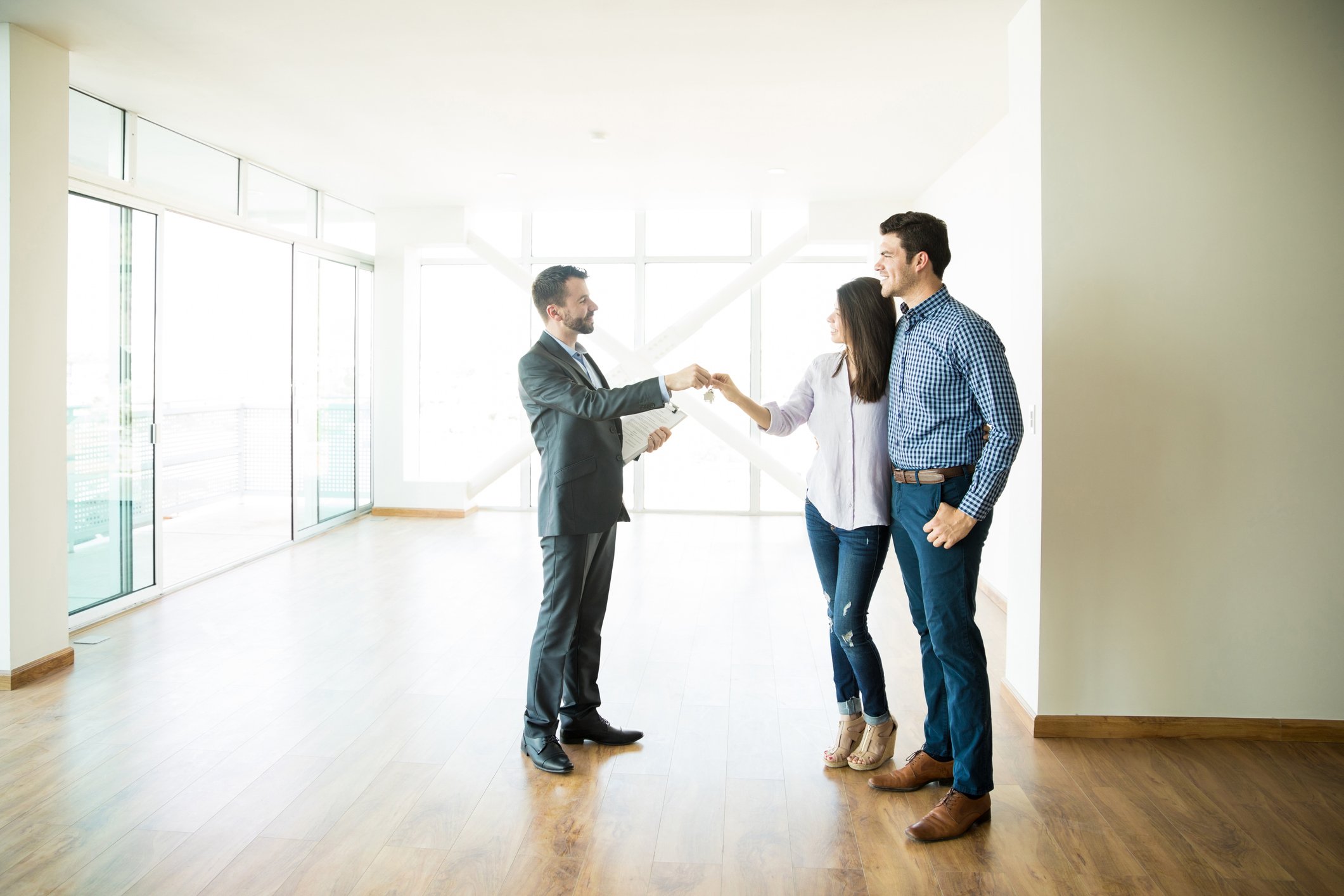 Man and woman in home with no furniture receiving keys from a man dressed in a suit