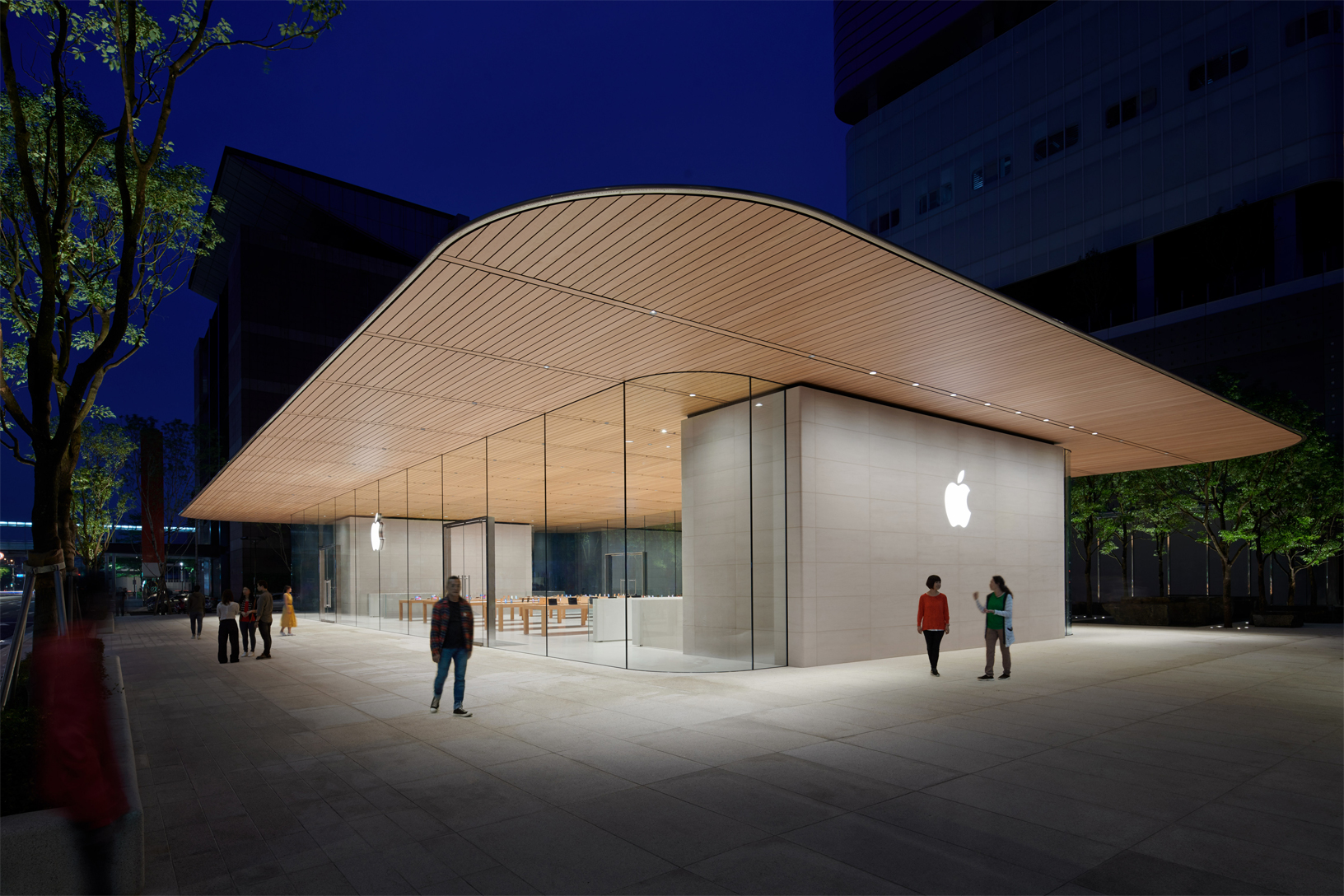 The new Apple store in Taipei with a wooden roof overextending the glass exterior and the white Apple logo displayed on the side of the building.