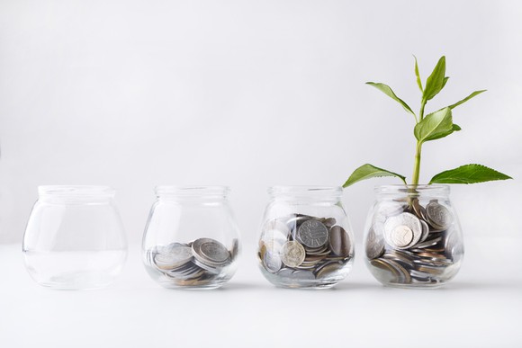 Four glass jars in a row, each filled with successively more coins and the last in the sequence having a plant growing out of it.