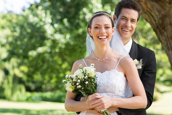 Smiling bride with bouquet of flowers standing in front of groom outdoors