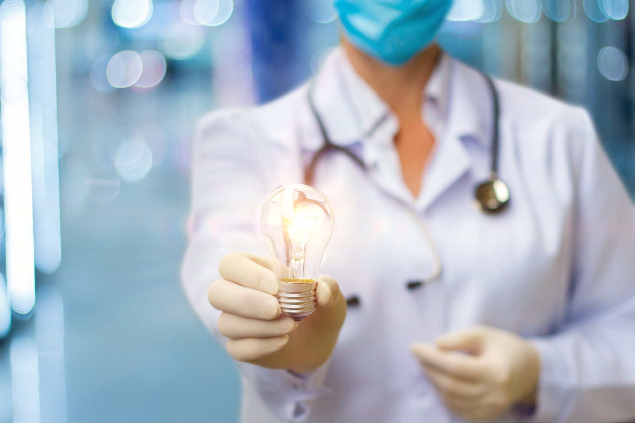 Doctor with gloved hands holding a light bulb.