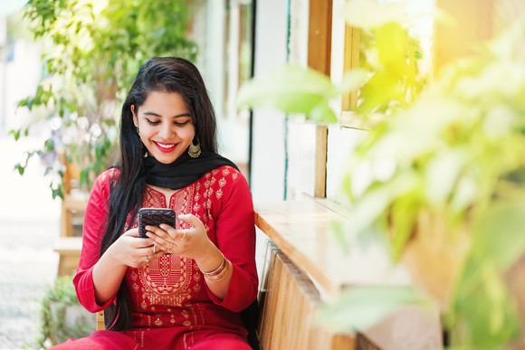 Young Indian woman in a bright red outfit looking at her phone.